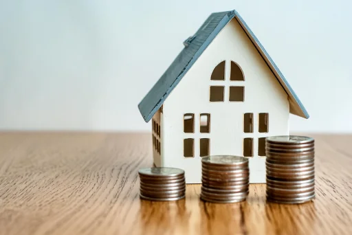 Baufinanzierung ohne Eigenkapital Ein kleines Haus mit 3 Münzstapeln davor