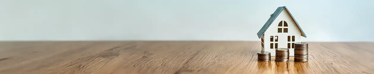 Miniaturhaus mit Münzen auf einem Holztisch