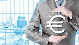 Mann der ein Eurozeichen in der Hand hält. Im Hintergrund ein Schreibtisch. 