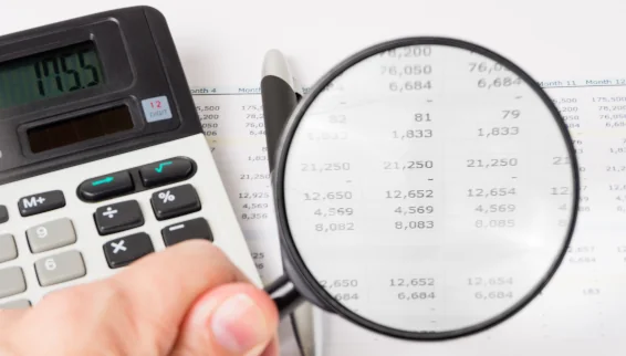 Ratgeber: Sondertilgung oder Festgeld anlegen: Was lohnt sich wann? Ein Taschenrechner liegt auf einem Tisch und eine Lupe vergrößert daneben Daten