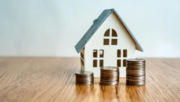 Vorfälligkeitsentschädigung bei einem Baudarlehen Modellhaus steht auf Tisch hinter Münzstapeln