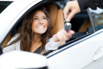 Eine Frau sitzt in einem Auto und nimmt einen Autoschlüssel entgegen