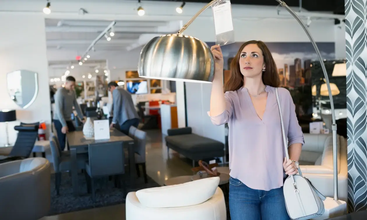 Frau begutachtet kritisch Preisschild einer Stehlampe im Möbelhaus Frau begutachtet kritisch Preisschild einer Stehlampe im Möbelhaus