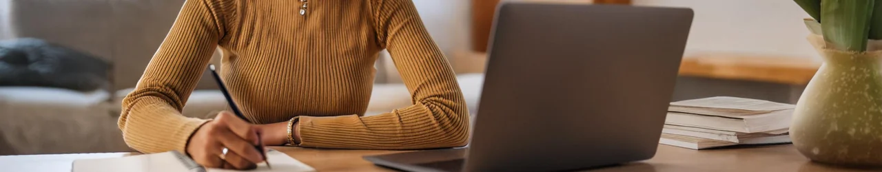 Frau sitzt an Laptop und notiert sich etwas