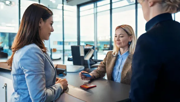 Welche Probleme können mit der Debitkarte im Ausland auftreten? Eine Frau führt mit ihrer Kreditkarte eine Mietwagenbuchung an einem Flughafen durch