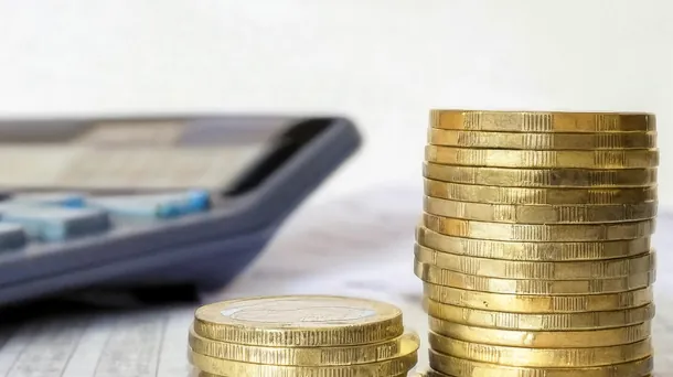 Definition und Grundprinzip der Quellensteuer Ein Stapel Münzen und ein Taschenrechner liegen auf einem Schreibtisch.