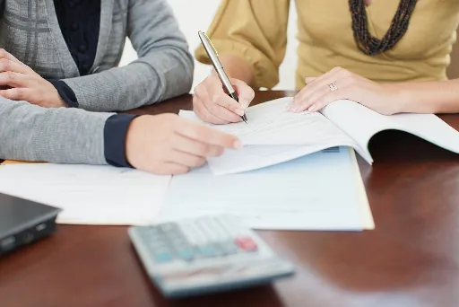 Zwei Personen sitzen an einem Schreibtisch und schreiben auf Papier