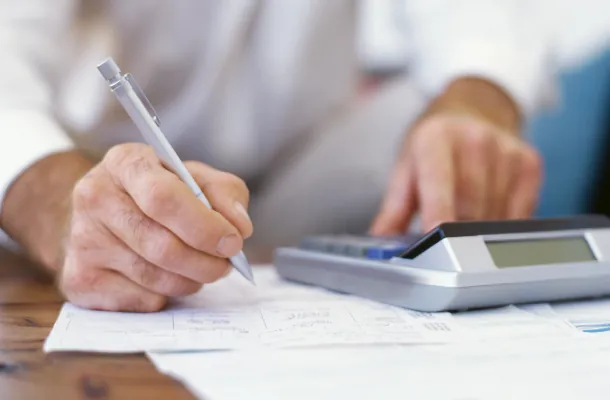 Eine Person schreibt mit einem Stift und tippt auf einem Taschenrechner