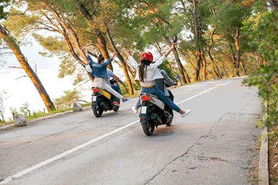 Vier junge Erwachsene fahren auf zwei Mopeds über eine Landstraße.