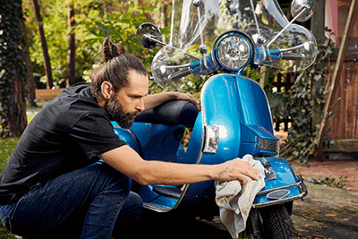 Ein Mann reinigt seinen blauen Roller.