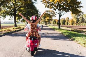 Ein Paar fährt im Sommer auf einem Roller durch die Landschaft.
