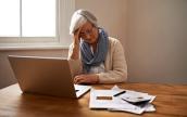 Eine Seniorin sitzt vor einem Laptop und hat Geldsorgen.