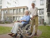 Älterer Mann schiebt Frau im Rollstuhl