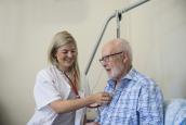 Pflegerin horcht mit Stethoskop älteren Mann ab.