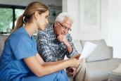 Pflegerin sieht Papiere mit älterem Mann im Wohnzimmer durch