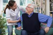 Eine Pflegerin hilft einem Senior aufzustehen.
