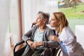 Seniorin im Rollstuhl und Pflegerin schauen aus dem Fenster.