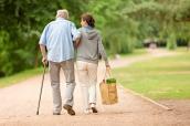 Senior geht mit junger Frau, die eine Einkaufstüte trägt, spazieren.
