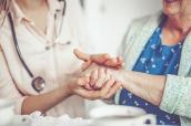 Pflegerin und Seniorin halten Hände.