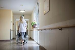 Eine Krankenschwester schiebt einen Rollstuhl durch einen Flur.