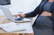 Schwangere Frau sitzt mit Laptop am Schreibtisch