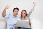 Eine Mann und eine Frau sitzen mit einem Laptop auf einem Sofa und jubeln.