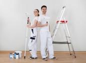 Mann und Frau stehen in Arbeitskleidung vor einer einer frisch geweisselten Wand.