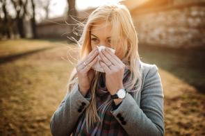 Eine junge Frau im Park hält sich ein Taschentuch vor die Nase.