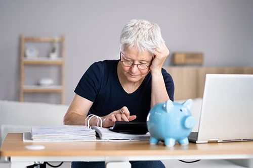Rentenbeitrag: Ältere Frau mit Taschenrechner, Aktenordner und Laptop