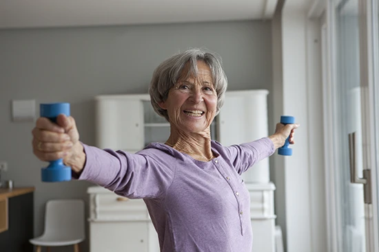 Rentenpunkte kaufen: Ältere Frau übt mit Hanteln in der Wohnung.
