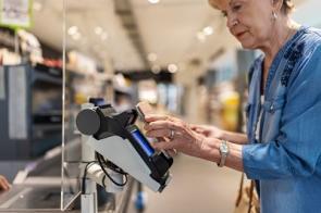 Ältere Frau zahlt an Supermarktkasse mit einem Handy.