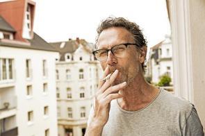 Rauchender Mann steht auf einem Balkon.
