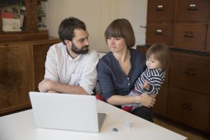 Eltern mit kleiner Tochter vor dem Laptop im Wohnzimmer