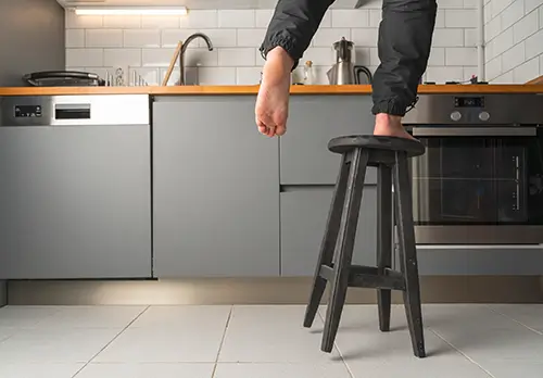 Ein Mann steht auf einem wackligen Hocker in einer Küche.