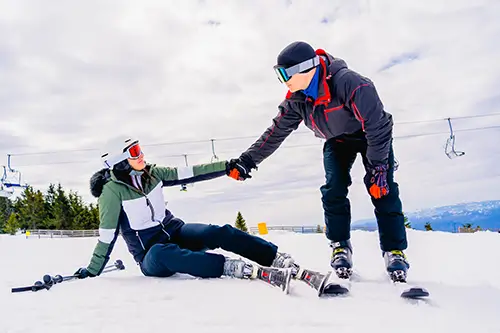 Skifahrer hilft gestürzter Skifahrerin auf der Piste