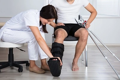 Ärztin legt einem Patienten eine Orthese an - Unfallversicherung für Sportverletzungen.