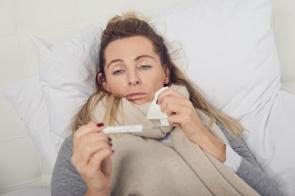 Frau liegt krank im Bett mit Fieberthermometer
