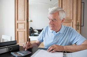 Älterer Mann mit Taschenrechner und Aktenordner in seiner Wohnung
