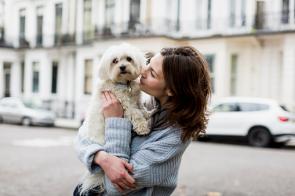 Eine Frau hält einen Hund auf dem Arm, sie stehen auf der Straße einer Stadt.