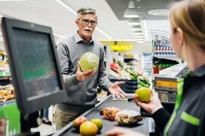 Älterer Mann spricht im Supermarkt mit einer Kassiererin.