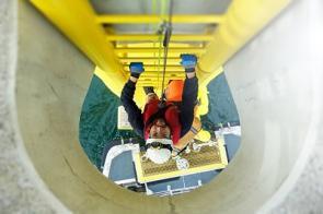 Arbeiter klettert Leiter an einer Offshore-Windkraftanlage hoch.