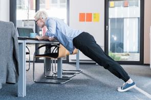 Angestellte macht Push-ups am Schreibtisch.