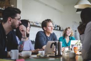 Junge Leute sitzen mit Laptops in einer Wohnküche.