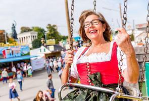 Eine fröhliche Rentnerin im Dirndl fährt mit einem Kettenkarussell auf dem Volksfest.