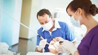 Ein Zahnarzt und seine Assistentin behandeln eine Patientin.