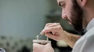 Ein Zahntechniker arbeitet mit einer Pinzette an einer Zahnkrone.