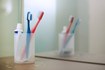 Ein Zahnputzbecher mit zwei Zahnbürsten und Zahnpasta im Bad.