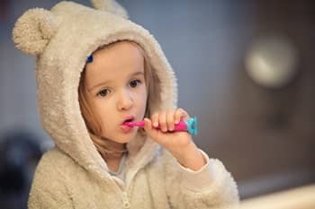 Ein kleines Mädchen in einem flauschigen Pullover putzt sich die Zähne.