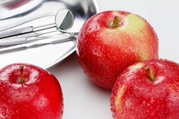 Drei rote Äpfel liegen neben Zahnarztutensilien.